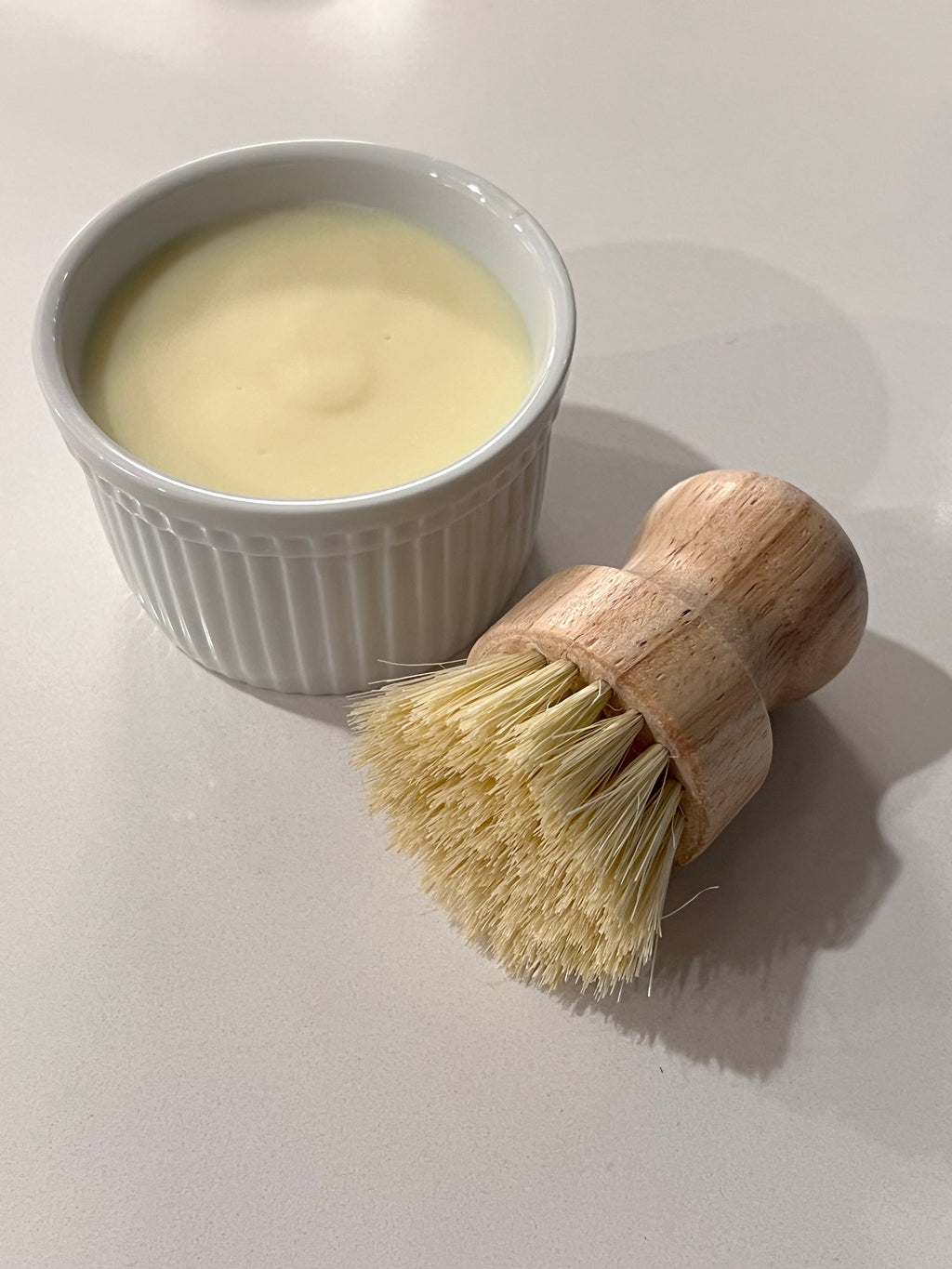 Natural handmade solid dish soap in a white ceramic bowl with a wooden dish brush